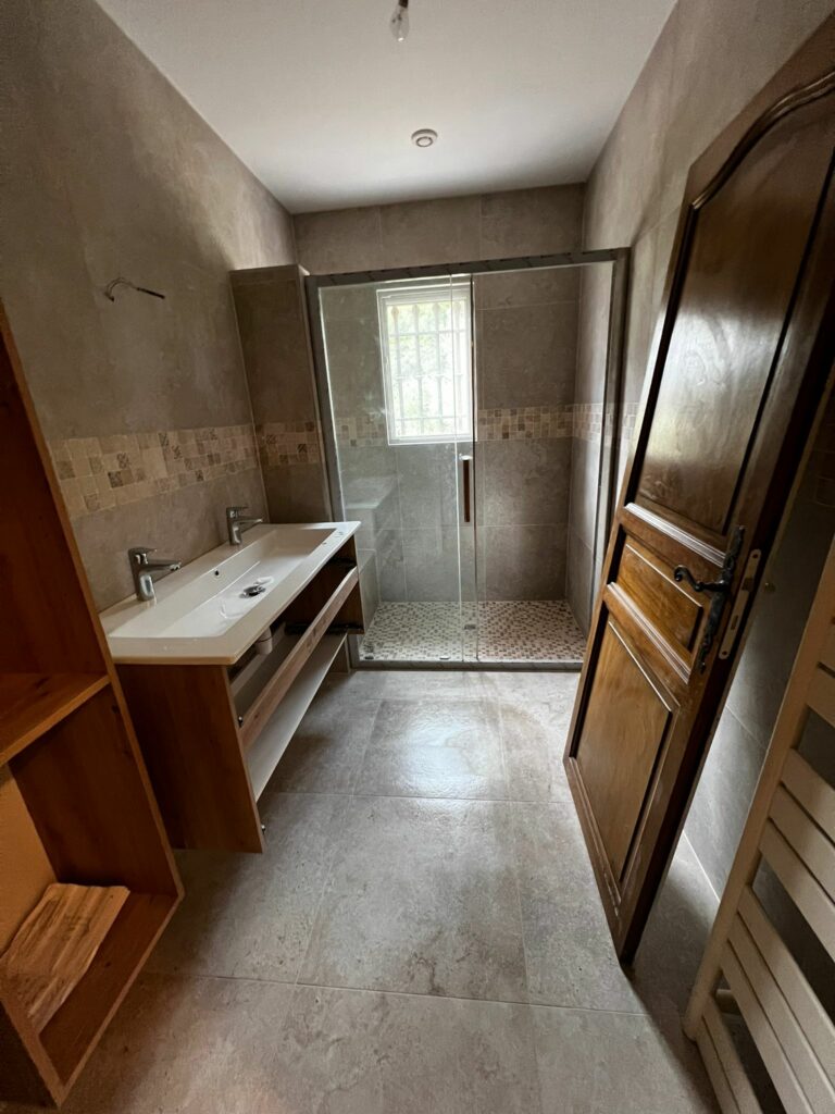Salle de bain Bravet à Caïs avec douche vitrée, double vasque et carrelage après travaux